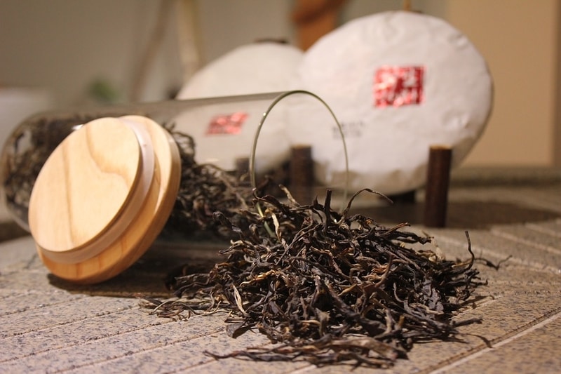 Loose leaf black tea leaves pouring out of a glass jar