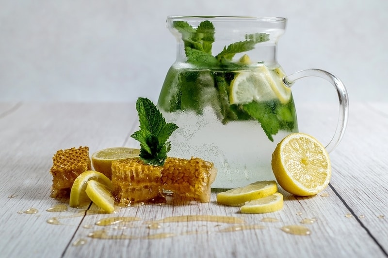Water pitcher with ingredients to make honey lemon tea surrounding
